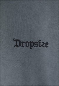 Grå sweatshirt med sort broderet tekst, der læser "Dropsize," med en struktureret stoffinish.