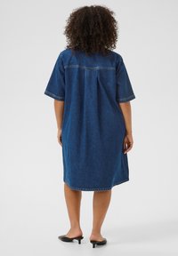 Robe en denim à coupe décontractée, à manches courtes et couture au dos. En bleu profond avec une apparence légèrement délavée, longueur genoux et fentes sur les côtés.