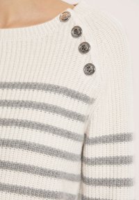 Weißer Strickpullover mit grauen horizontalen Streifen und vier dekorativen silbernen Knöpfen an der Schulter, mit einem gerippten Halsausschnitt und strukturiertem Stoff.