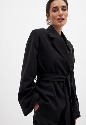 Zwarte blazer van gladde stof, met een brede kraag, lange mouwen en een ceintuur in de taille met een ruime pasvorm.