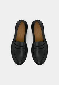 Μαύρα δερμάτινα μοκασίνια με λείο φινίρισμα, που διαθέτουν ραμμένο σχέδιο και λεπτομέρεια με άνοιγμα για πένυ στο μπροστινό μέρος. Ορατή ταμπά εσωτερική επένδυση.