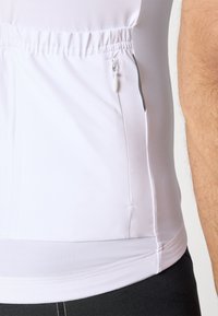 T-shirt de sport blanc à manches courtes avec taille élastique ; il présente une poche latérale zippée, une texture lisse et des coutures minimales pour le confort.