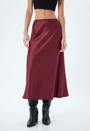 Gonna maxi in satin borgogna con una texture morbida, vita aderente e design fluido, abbinata a stivali neri con tacco.