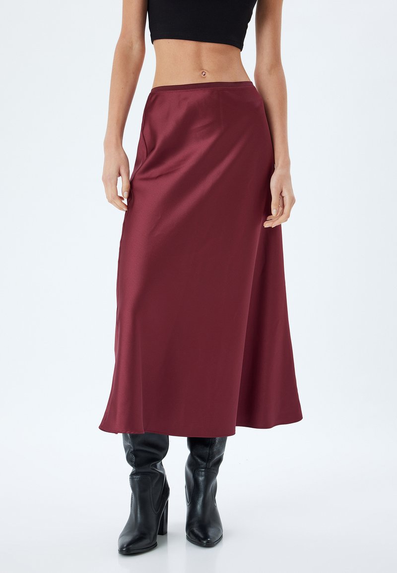 Gonna maxi in satin borgogna con una texture morbida, vita aderente e design fluido, abbinata a stivali neri con tacco.