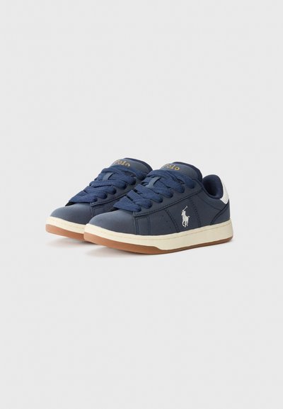 Marinblå sneakers tillverkade av syntetiskt material, med en vit häl, gummisula och snören. Logotyp syns på tungan och sidan.