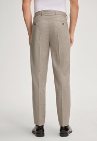 Beżowe spodnie w kratę o dopasowanym kroju, z dwoma tylnymi kieszeniami z guzikami i prostą nogawką, w zestawie z czarnymi butami.