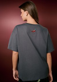 Grijs katoenen T-shirt met korte mouwen, met een kleine rood-groene geborduurde chilipeper bij de halslijn aan de achterkant.