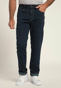 Granatowe dżinsy o slim fit z przednimi kieszeniami, zapięciem na guzik i podwiniętymi mankietami. W połączeniu z białymi trampkami.