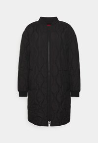 Veste matelassée noire avec fermeture éclair, col et poignets côtelés, et une coupe mi-longue présentant un motif ondulé texturé.