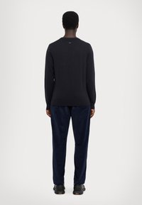 Black wool sweater with long sleeves, ribbed cuffs and hem, worn with navy velour pants. Smooth texture and simple design.