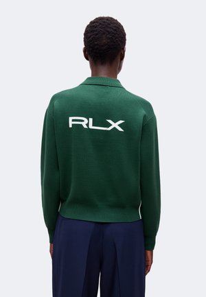 Isik, kes kannab tumerohelist pika varrukaga särk-topp, millel on seljal valge RLX logo, ning tumesiniseid pükse, seljaga vastu tavalist tausta.