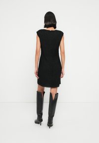 Μαύρο, αμάνικο φόρεμα με υφή, χνο υδωτό ύφασμα, με ραφή στην πλάτη και στρογγυλή λαιμόκοψη. Συνδυάζεται με μαύρες μπότες μέχρι το γόνατο.