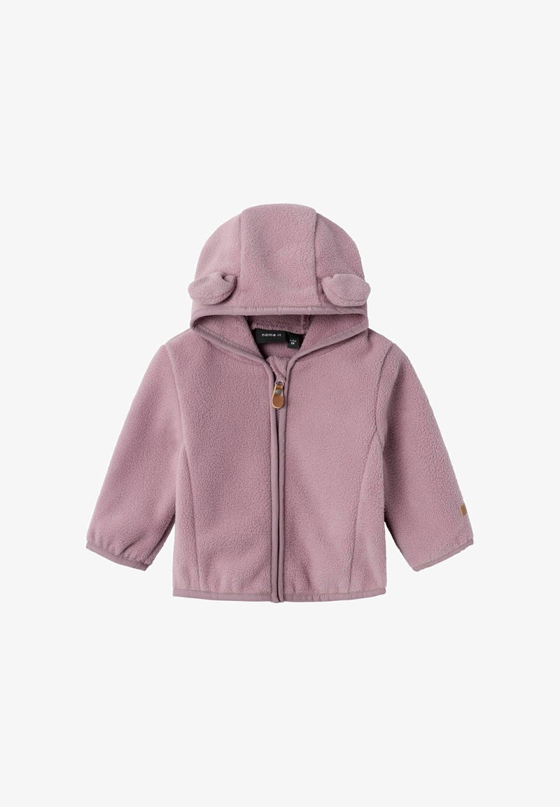 Veste en polaire rose pâle avec une capuche dotée d'oreilles d'ours, fermeture éclair à l'avant et finitions contrastantes. Manches longues et sans poches.