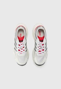 Scarpe da corsa bianche con accenti rossi, strisce grigie e texture in rete. Presentano un collare imbottito e lacci sopra la linguetta. Progettate per il comfort.