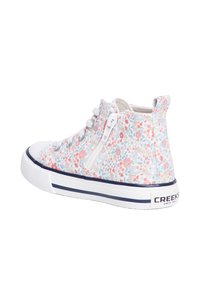 Zapatillas altas con un patrón de tela blanca con flores, cordones grises y un zipper lateral. Presentan una puntera de goma y suela blanca con acentos azules.