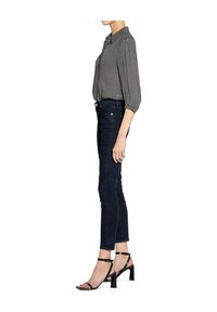 Black and white patterned blouse with a collar, paired with dark jeans and black block-heeled sandals. Side view shows fitted design.