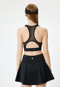 Svart atletisk crop top med racerback-design och genomskinliga mesh-paneler, kombinerad med en utsvängd svart kjol med en mjuk midja.