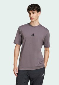 Maglietta grigia a maniche corte realizzata in tessuto morbido, con un piccolo logo Adidas nero sul petto, dalla vestibilità rilassata e colletto rotondo.