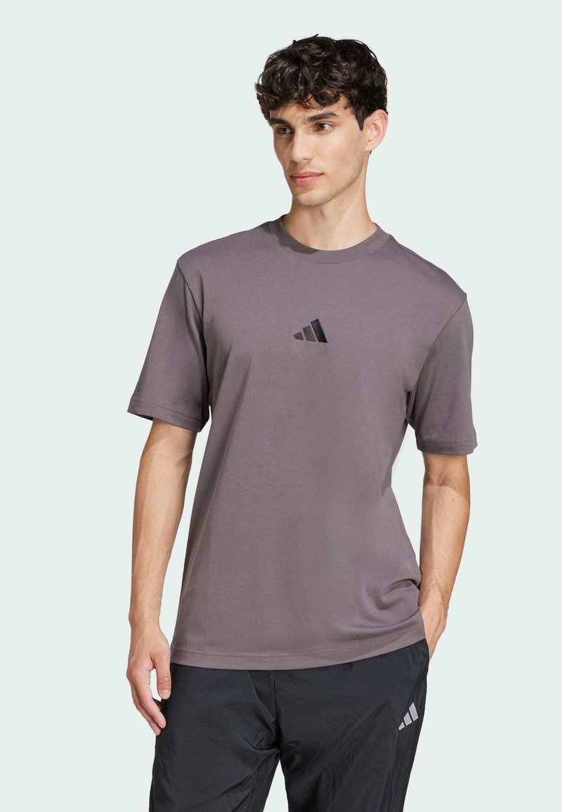 Maglietta grigia a maniche corte realizzata in tessuto morbido, con un piccolo logo Adidas nero sul petto, dalla vestibilità rilassata e colletto rotondo.