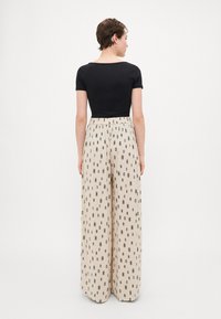 Black fitted top paired with wide-leg beige pants featuring a black geometric pattern, with an elastic waistband and lightweight fabric.