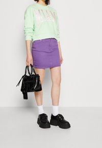 Sweatshirt verde menta con grafica "MIAMI", gonna di jeans viola, calzini bianchi, scarpe platform nere e una piccola borsa nera lucida.