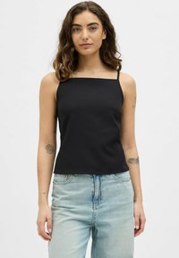 Musthave musta ilma varrukatega tops, mis on valmistatud siledast kangast. Omab ruudukujulist dekolteed ja pinguldavat siluetti, koos helesiniste kõrge vöökohtadega teksadega.