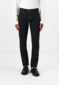 Fekete farmernadrág slim fit fazonban, öt zsebbel, �övhurkokkal és gombos zárással. Hosszú ujjú fehér inggel és fekete cipővel viselve.