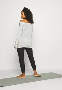 Felpa grigia chiara a spalle scoperte con maniche lunghe e polsini a costine, abbinata a pantaloni jogger neri a gamba affusolata. Texture morbida, design minimale.