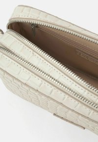 Bolso de crema con textura de cocodrilo, cuenta con dos compartimentos con cremallera y herrajes metálicos. El interior presenta un forro beige liso.