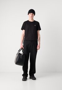 Svart t-skjorte med kort erme og logo, vide svarte bukser, svart lue, og svart lærveske. Skoene er svarte joggesko.
