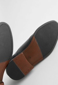 Must tõmblukkadega must nahkne king, millel on pruun tekstuuriga konts. Kõrgus on tõeline mustriline disain, mis tagab hea haarde. Ülemine osa on kaunistatud wingtip stiili detailidega.