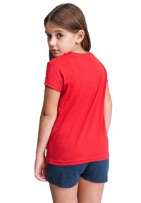 Camiseta de algodón roja con mangas cortas, neckline redondeado y una textura suave, llevada con pantalones cortos azules. La vista desde atrás muestra un diseño simple.