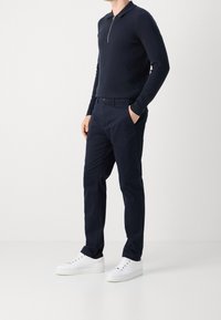Polo a maniche lunghe blu navy con colletto a zip, abbinato a pantaloni blu navy e sneakers bianche, che mostrano un design casual e lineare.