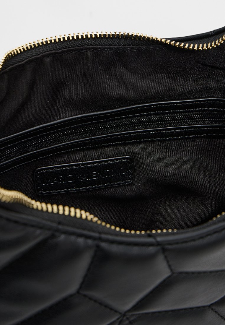 Interior de un bolso de cuero acolchado negro con un zipper dorado, forro de tela negra, un bolsillo interno con cremallera y una etiqueta de marca cosida en el interior.