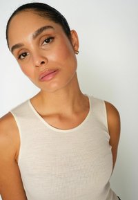 Light beige ribbed tank top with a rounded neckline and narrow straps. Smooth texture and minimalistic design, suitable for layering.