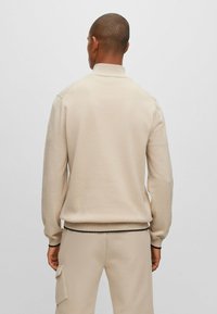 Beige stickad tröja med hög krage, ribbad mudd och nederkant. Slät textur, åtsittande siluett, minimalistik design utan dekorationer.