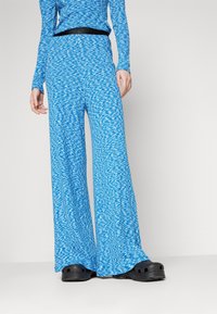 Blue patterned wide-leg pants made from a textured fabric, with a black waistband. Paired with black slip-on shoes, showcasing a relaxed look.
