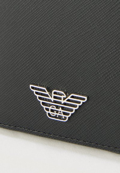 Fekete, texturált bőr pénztárca ezüst színű, szárnyas "GA" betűs logóval. A kialakítás tiszta vonalakat és minimalista esztétikát tartalmaz.