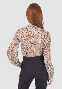 Blusa trasparente a maniche lunghe in stampa leopardata con colletto punta, abbinata a pantaloni a righe verticali a vita alta, che evidenziano un design moderno.