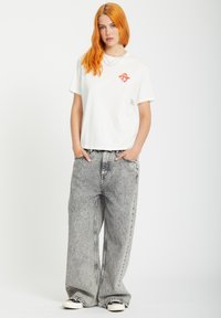 White cotton t-shirt featuring a red rolling lips graphic, paired with oversized gray denim jeans and black sneakers. Simple, casual design.