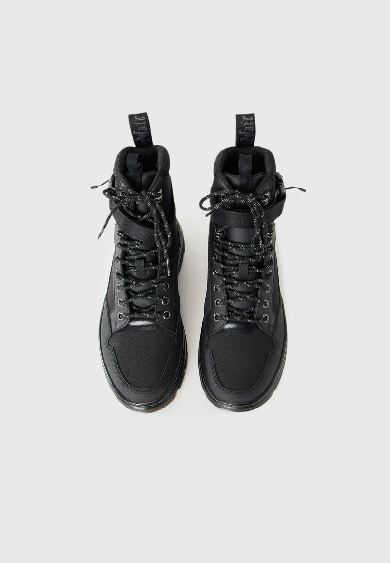Une paire de baskets montantes noires avec des lacets à motifs et des sangles à la cheville, vues de dessus sur un fond blanc.