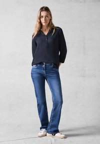 Marineblauw overhemd met driekwartmouwen, gecombineerd met lichtblauwe denim jeans. Casual witte sneakers maken de outfit compleet.