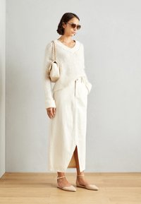 Pull en tricot crème avec décolleté en V, associé à une jupe en denim beige clair avec une fente à l'avant. Ballerines beiges pointues et un petit sac à épaule.