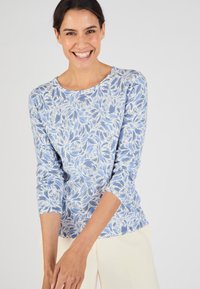Maglietta a maniche lunghe azzurro chiaro con un motivo floreale in bianco e tonalità di blu scuro; scollatura rotonda e texture morbida del tessuto.
