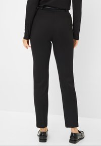Zwarte tapered broek met een zachte textuur, voorzien van een hoge tailleband en een slanke silhouet. Gekocht met glanzende zwarte schoenen.