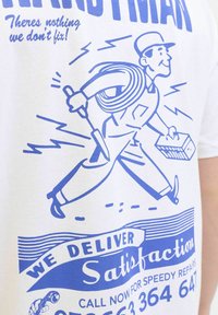T-shirt blanc avec un graphisme de bricoleur de style cartoon en bleu, tenant des outils avec une boîte à outils, et le texte : « NOUS GARANTISSONS votre satisfaction. »