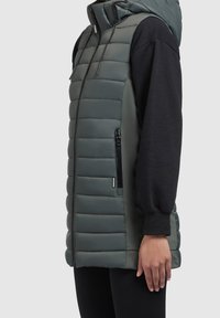 Gilet imbottito verde scuro con texture liscia, tasche laterali con cerniera e cappuccio. Presenta cuciture verticali e una vestibilità comoda.