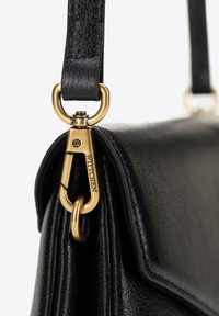 Bolso de mano de piel negra con una superficie texturizada, un cierre de hardware dorado y una correa de hombro con un anillo metálico prominente.