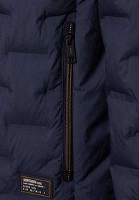 Ciemnoniebieska kurtka puchowa z kieszenią na zamek błyskawiczny na klatce piersiowej oraz prostokątną, czarno-brązową metką z napisem "NORTHERN EXPO" oraz szczegółami współrzędnych.