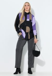 Czarna koszula na guziki z geometrycznymi wzorami w kolorach fioletowym, beżowym i czarnym; połączona z szarymi, dopasowanymi spodniami i małą czarną torebką.